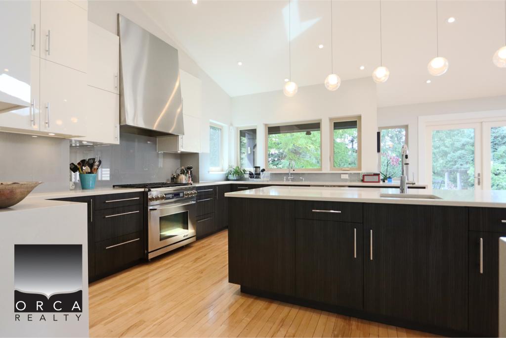 Spacious, contemporary kitchen featuring a large island, sleek black and white cabinetry, and abundant natural light from multiple windows, ideal for modern home living.