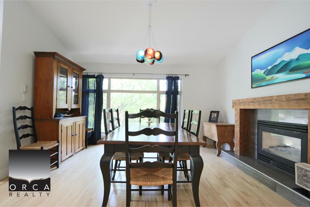 Spacious dining area featuring a wooden table, six chairs, a fireplace, and a large window with blue curtains, perfect for family gatherings and entertaining guests.