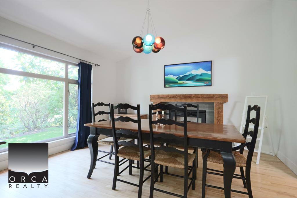 Spacious dining room featuring a large window with natural light, a wooden dining table, six black chairs, and a modern chandelier, creating a welcoming and stylish space.