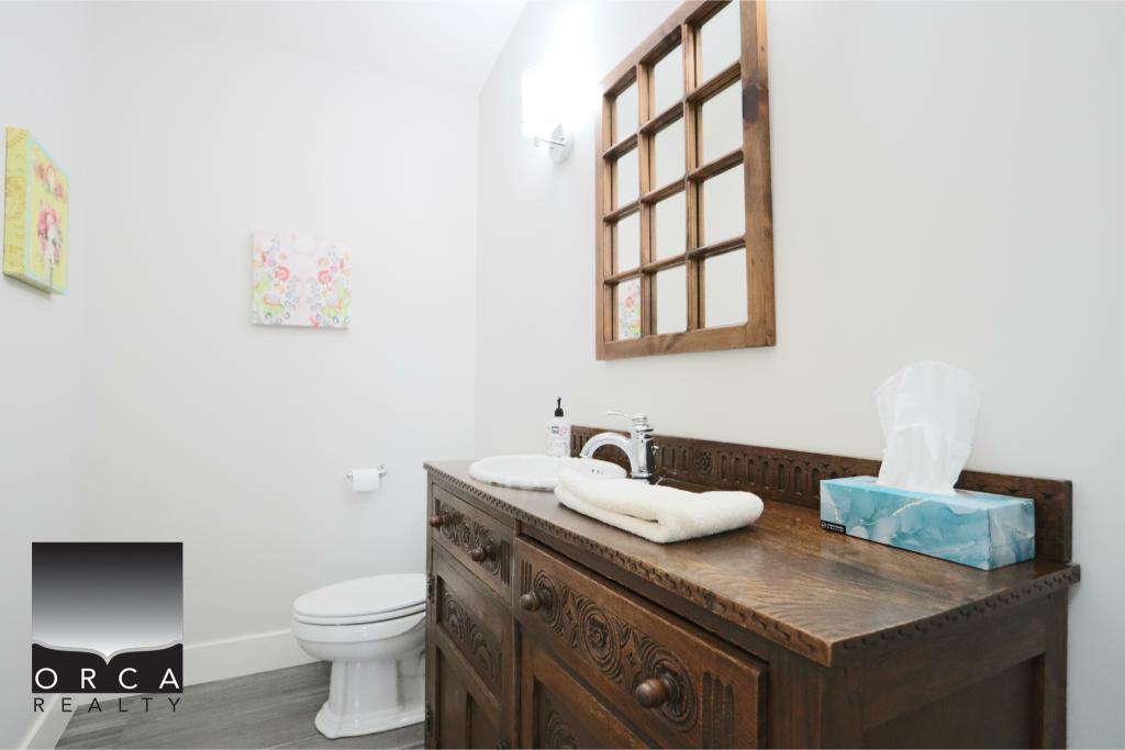 A clean, modern bathroom featuring a vintage wooden vanity with a white countertop, a toilet, and a decorative wooden window frame, creating a cozy and stylish space.