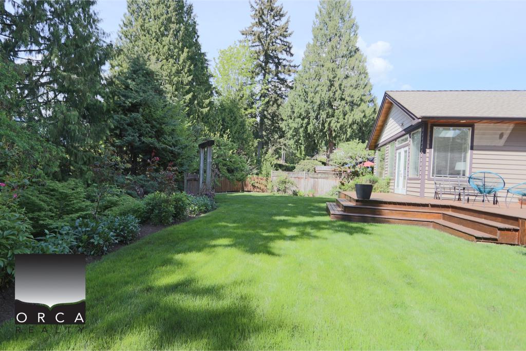 Lush backyard with well-maintained grass, garden, and outdoor deck in Victoria, BC, ideal for outdoor living and relaxation.