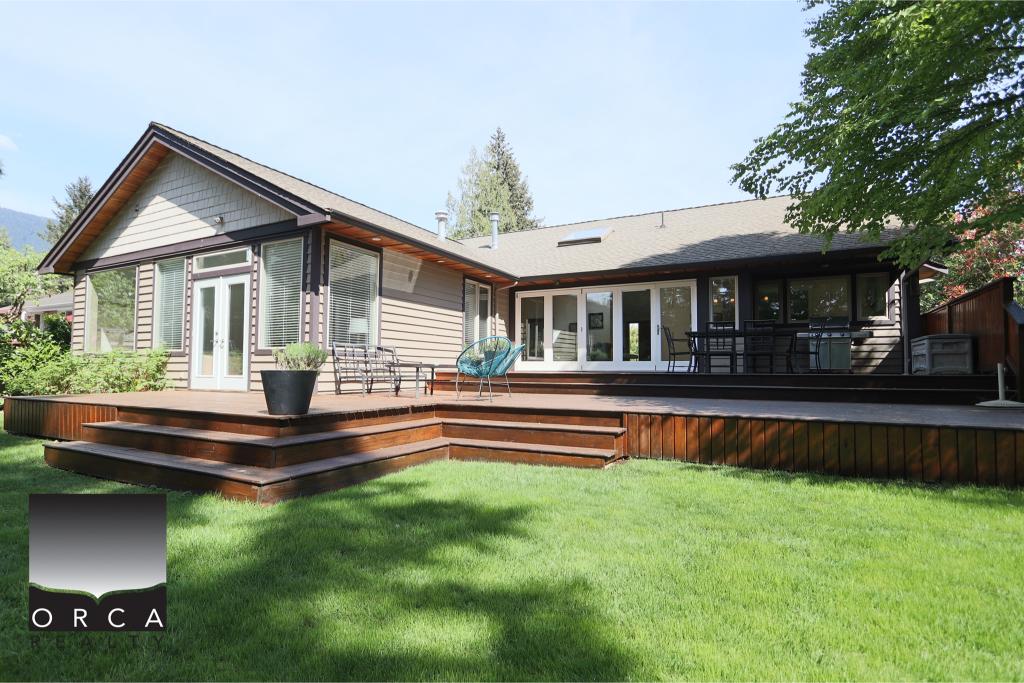 Beautiful modern craftsman-style home featuring a large wooden deck, surrounded by lush green lawn and mature trees, ideal for outdoor living and entertaining.