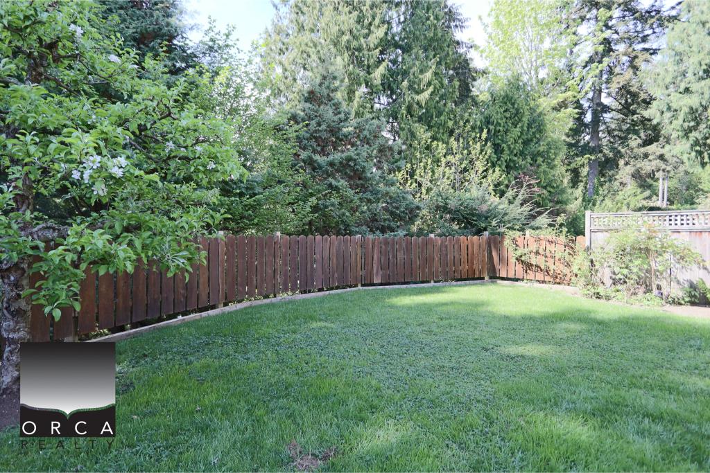 Bright, well-maintained backyard featuring a green lawn and mature trees, enclosed by a sturdy wooden fence, ideal for outdoor activities and family gatherings.