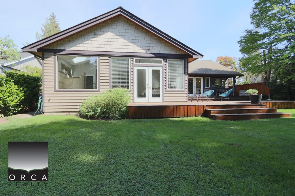 Bright and inviting suburban house with large windows and a wooden deck, surrounded by lush green lawn and mature trees, ideal for family living and outdoor entertaining.
