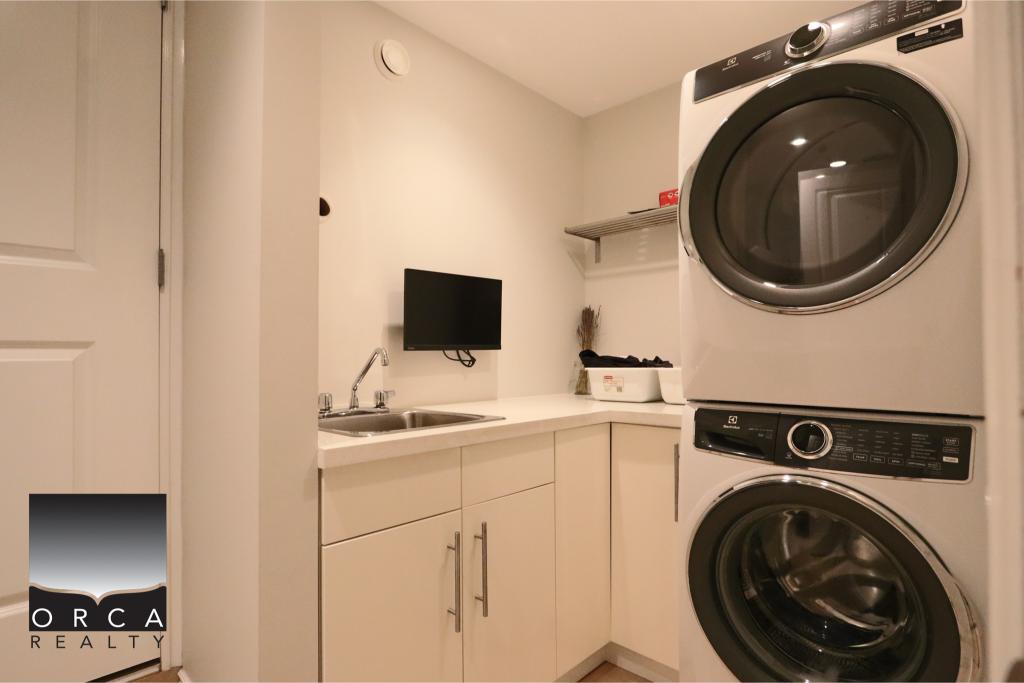 Bright laundry room featuring stacked washer and dryer with white cabinetry and a small wall-mounted TV for convenience.