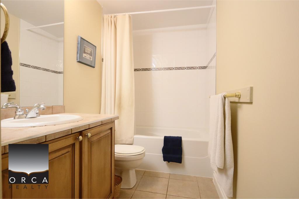 Bright bathroom featuring a bathtub, shower curtain, toilet, and wooden vanity with sink, ideal for Vancouver-area homes.