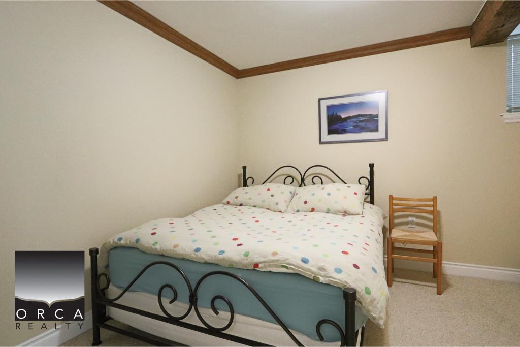 Comfortable bedroom featuring a metal bed frame, colorful polka dot bedding, a wooden chair, and a framed landscape photo on the wall, ideal for a relaxing home environment.