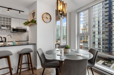 A detailed, modern kitchen and dining area in a high-rise apartment with large windows, city views, and contemporary decor, showcasing urban living and real estate in Vancouver.