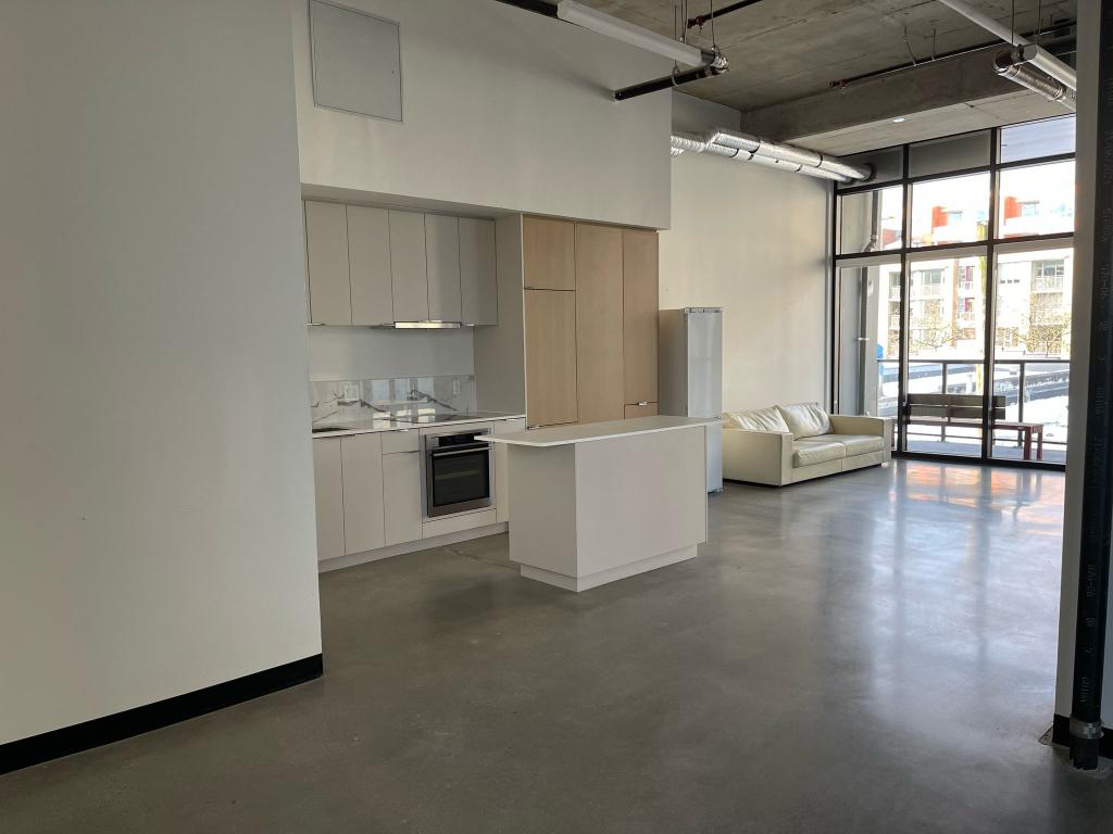 Spacious modern condo interior in Vancouver with open kitchen and large windows offering city views.