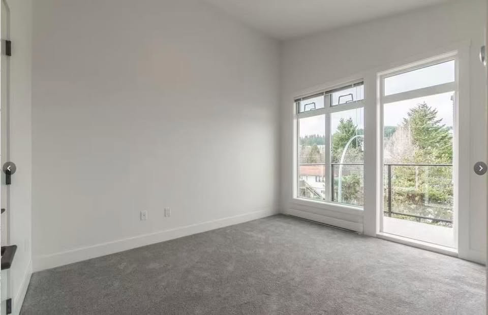 Empty room with large windows and sliding glass door, natural light, neutral walls, and carpeted floor in Nanaimo property.
