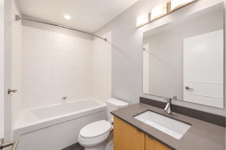 Contemporary bathroom featuring a bathtub, toilet, and vanity with a large mirror, illuminated by modern lighting, in a clean and minimalist style.